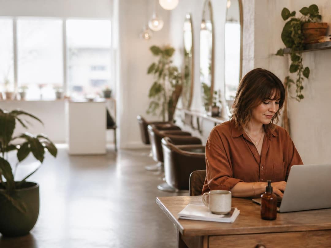 Salon owner working at a laptop at a small desk in the corner of her salon
