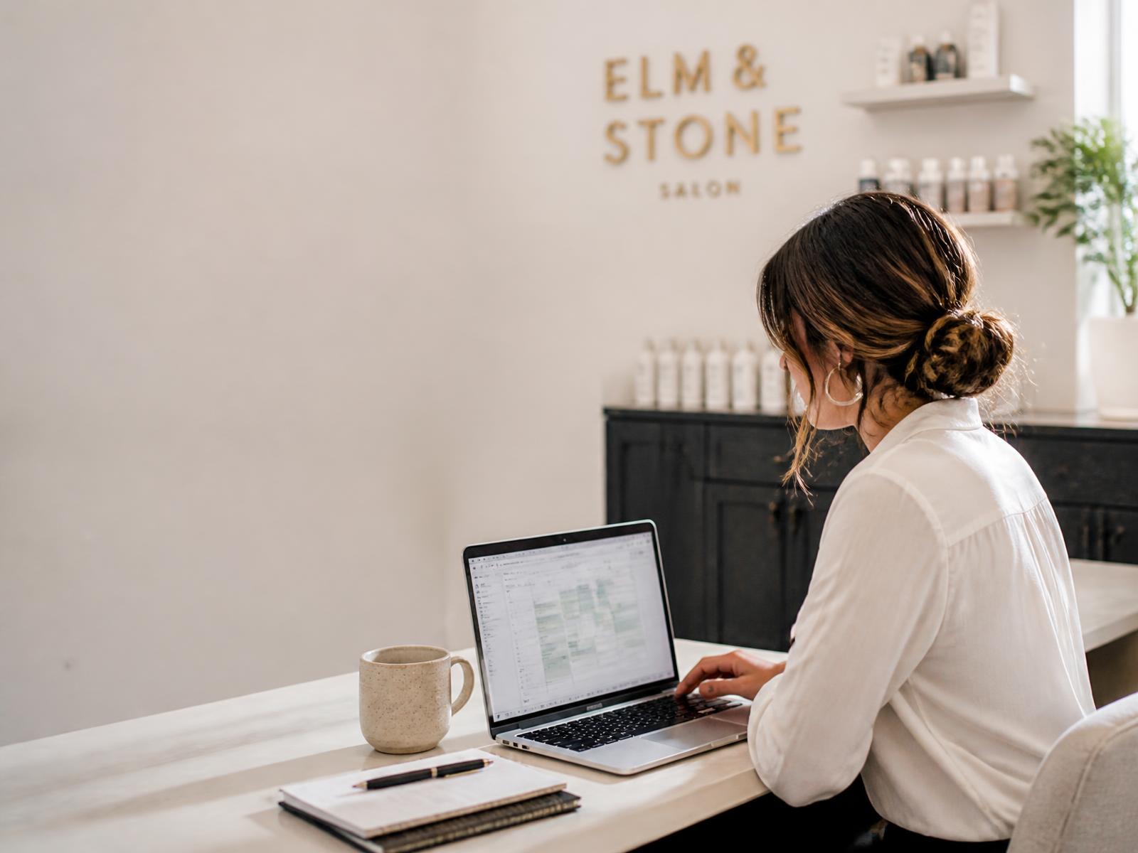 Salon owner at a laptop in the back office reviewing her booking rules